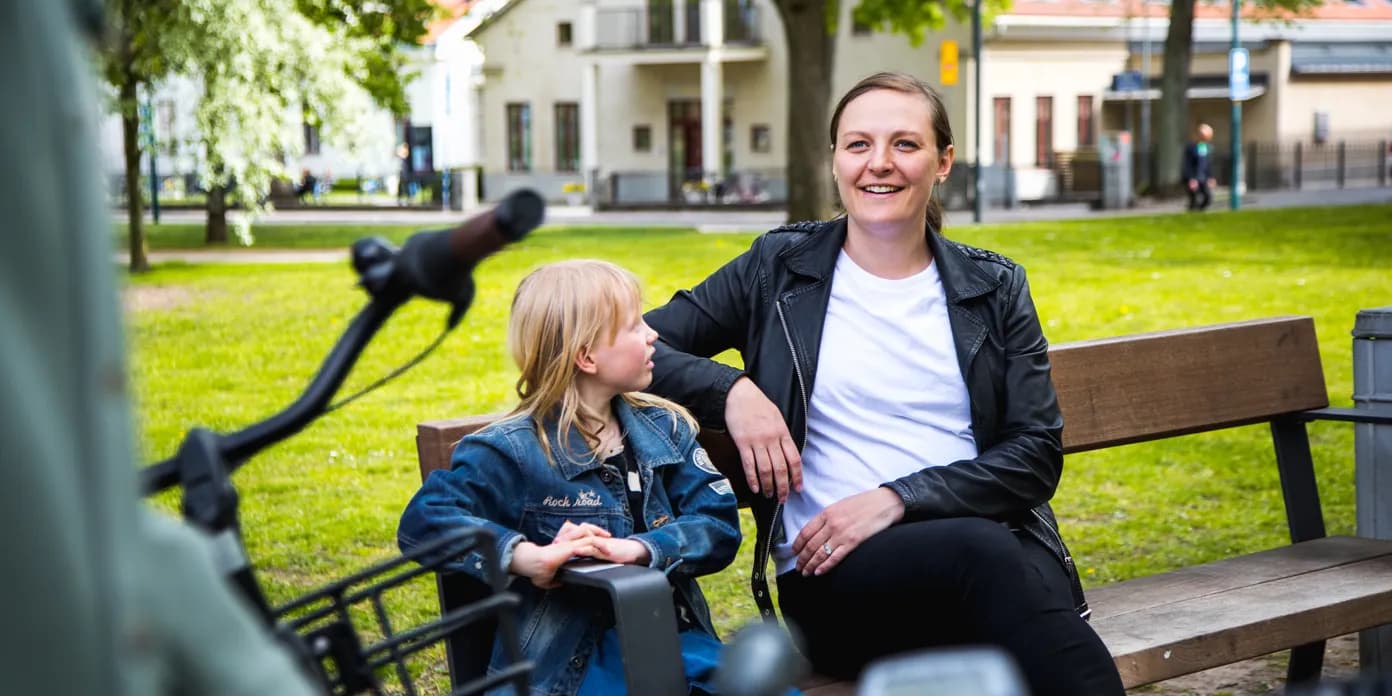 En kvinna sitter på en bänk bredvid en liten flicka