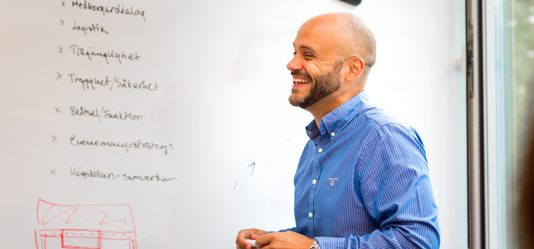 En person som ler och står framför en whiteboard med text