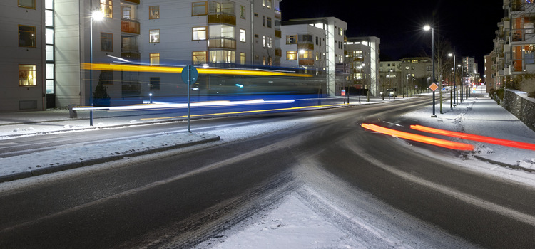 En gata i Skövde fotad en mörk vinterkväll med snötäckta gator. Man ser bara ljuset av bilar och en buss som åker förbi. 